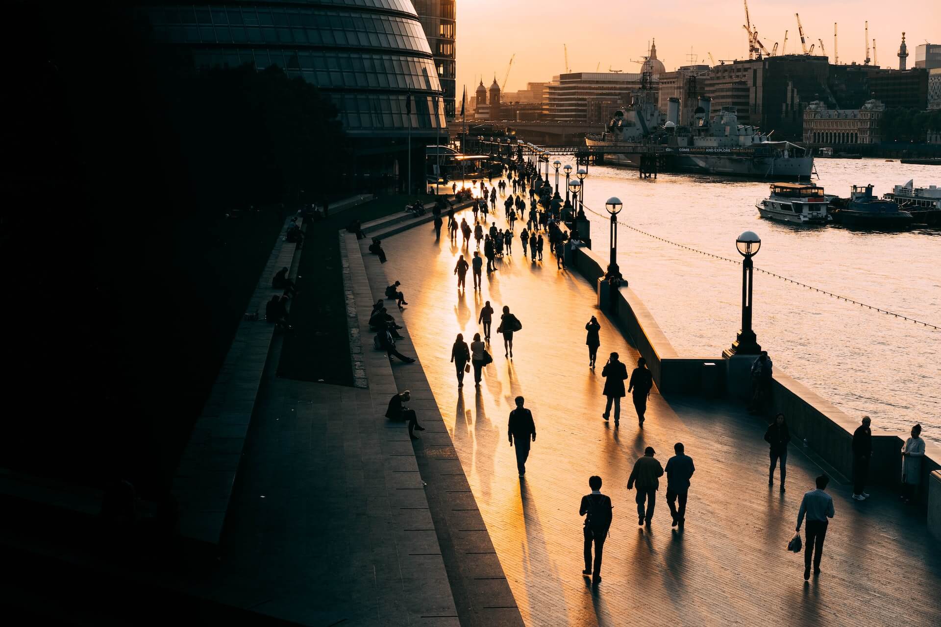 People walking alongside the River Thames in London as the sun sets.